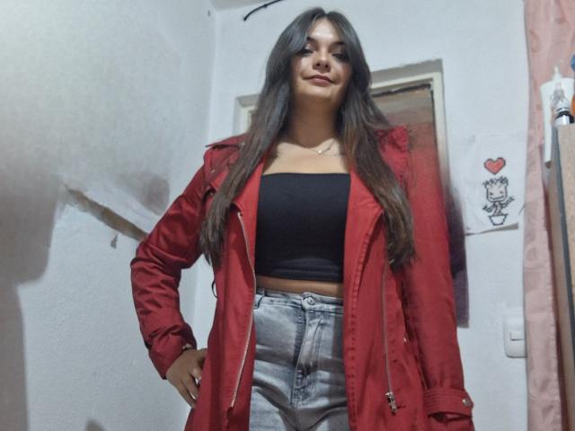 katherinLatin with long brown hair, red jacket, black tube top, and high-waisted jeans, standing confidently, hands on hips, slight smile, small necklace, medium tits, cute.