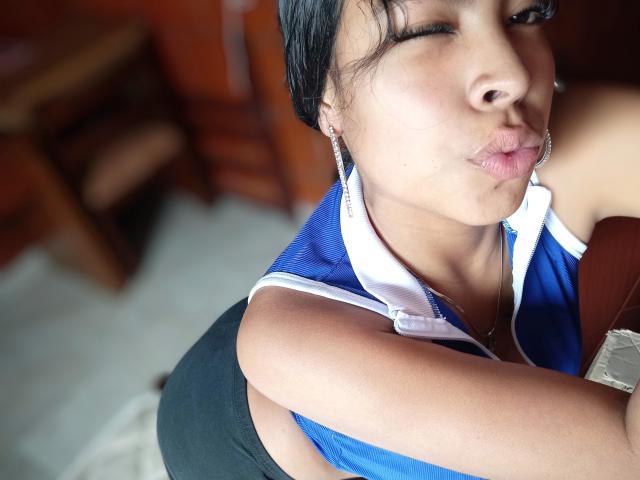 SashaLia with pouty lips, wearing a blue and white sports top, black shorts, and silver earrings, showing her medium-sized tits and slightly visible ass. Her eyes are closed.