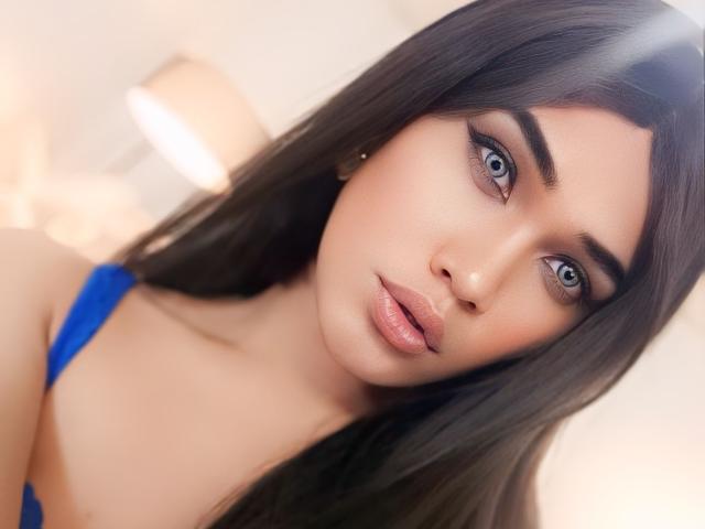 AlluringAmelia with blue eyes, full pink lips, and long dark brown hair, wearing a blue top, looking directly at the camera with a soft, alluring expression.