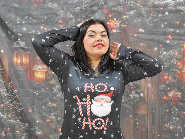FantasykLadies with black snow-patterned sweater, "Santa" and "Ho Ho" graphic, hands in hair, smiling, red lipstick, black hair, medium build, snowflakes, Christmas-themed backdrop.