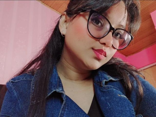AzulMoon tiene la piel de un marrón medio, cabello negro largo, usa gafas negras gruesas, una chaqueta vaquera y lápiz labial rosa, con un ligero puchero, en un selfie..