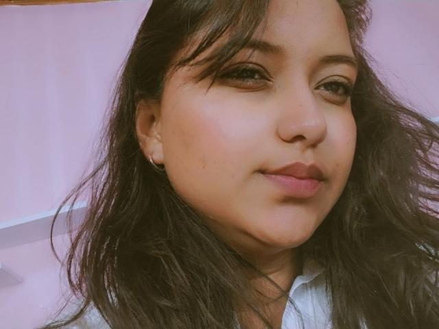 AzulMoon, com cabelos longos e escuros, pele clara, maquiagem discreta e um leve sorriso, vestindo uma camisa branca, mostrando uma pequena marca de beleza abaixo do olho direito..