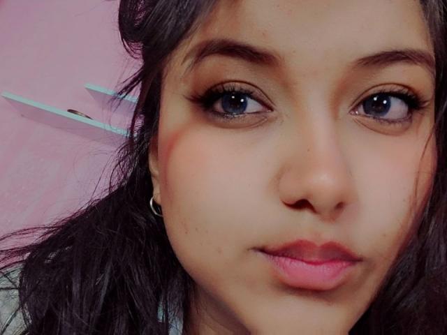 AzulMoon's face, showing large blue eyes, dark wavy hair, and pink lips with a slight pout. She has a light brown skin tone and small, dark earrings.