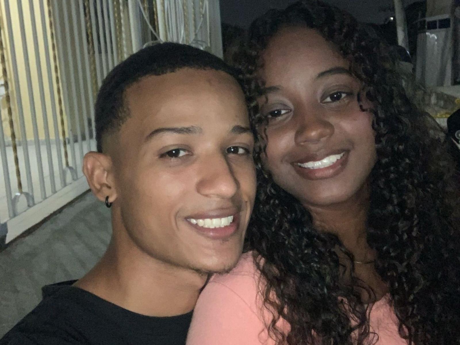 AngelaAndMarcos with short black hair and black shirt, smiling, next to AngelaAndMarcos with curly brown hair and pink shirt, both showing white teeth in a selfie.