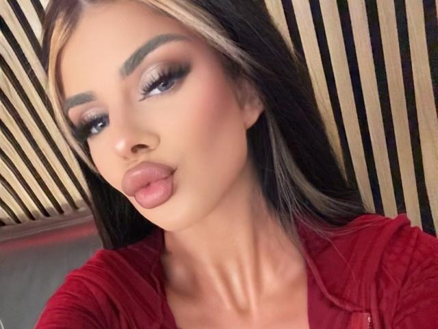 IvyRaven has pouty lips, heavy eyeliner, and long, straight blonde hair with dark roots. She's wearing a red shirt, looking directly at the camera.