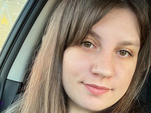 ToniElizabeth's face, brown eyes, and straight brown hair in a car, slight smile, small pimple on right cheek, light skin, no makeup, subtle natural beauty, soft pink lips.