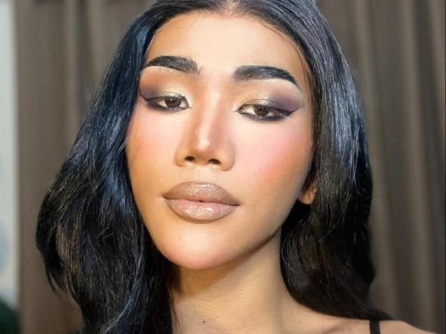 JasmineCole has glossy black hair, full eyebrows, smokey eye makeup, pink blush, and shiny nude lipstick. She's staring forward with a neutral expression.