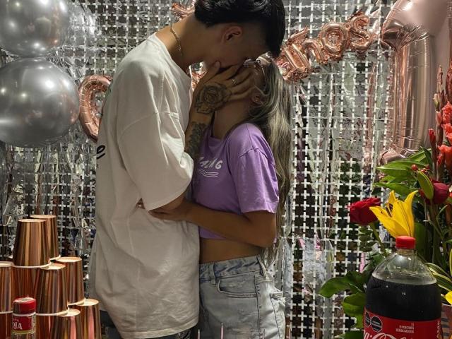 KataAndByron kissing, KataAndByron's hand on Byron's face, Byron's white tee, KataAndByron's purple tee, denim shorts, tattoos, silver balloons, pink metallic numbers, red flowers, soda bottle.