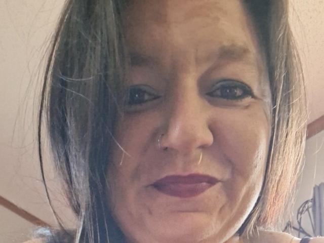 Keeker69 has medium-length brown hair, a nose ring, and dark red lipstick. She's smiling with slightly wrinkled skin and dark eyeliner. Her tits are not visible in the image.
