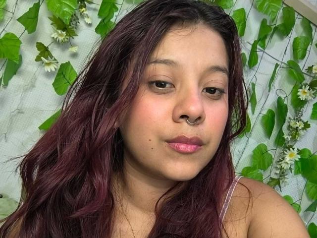 CoralineHale has wavy dark red hair, a nose ring, and pink lipstick. She's looking at the camera with a slight pout. Her tits are not visible.