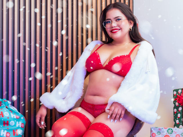 LilyRousee, curvy, in red lingerie with cut-out bra, red panties, red thigh-highs, white fur jacket, glasses, smiling, dark hair, red lipstick, sitting, snowflakes, Christmas bag.