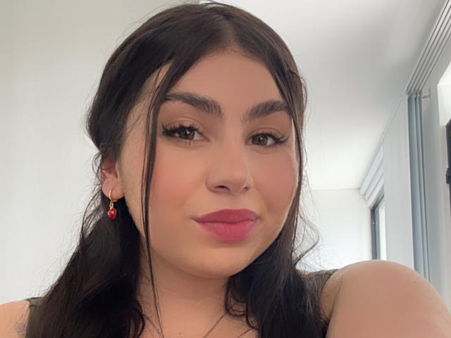 VenusxMusa has pouty pink lips, dark brown eyes with long lashes, and black hair with loose strands. She's wearing red earrings and has a light skin tone.