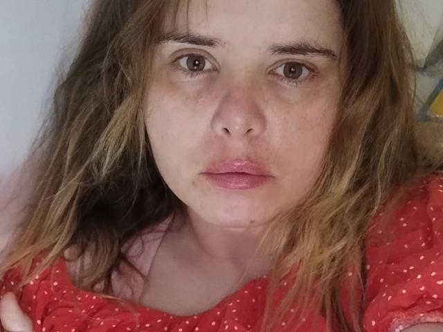 ElenaSchatz-hot has brown eyes, slightly parted pink lips, and wavy blonde-brown hair. She's wearing a red polka-dot shirt, looking directly at the camera with a neutral expression.