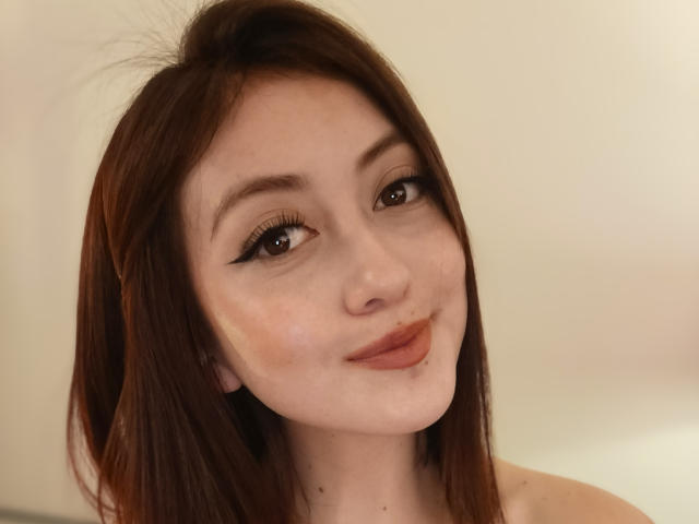 AngelaTorres has brown hair, brown eyes, and a slight smile with a subtle pout. She's looking up with a cute, soft expression and light makeup.