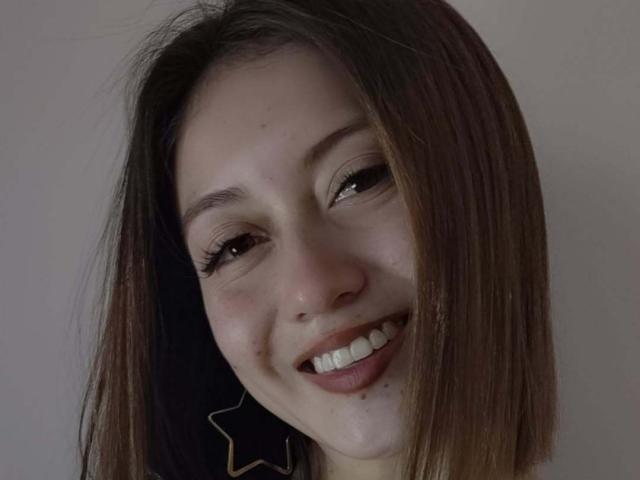 AngelaTorres has a cute smile with white teeth, brown eyes, and straight brown hair. She's wearing star-shaped earrings and has a few freckles on her face.