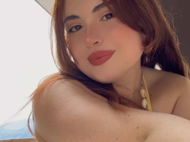 VicluX has red lips, light skin, and brown hair, wearing a yellow halter top with shell beads, looking at the camera with a slight smile. Her tits are partially visible.