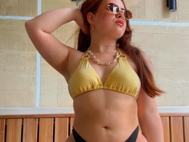 VicluX with red hair, glasses, yellow bikini top, chain necklace, black panties, wooden wall, hand in hair, confident, sexy, medium tits, curvy, attractive.