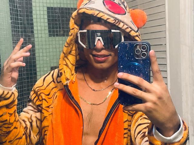 DaironLee with tiger hoodie, orange vest, virtual reality headset, and blue glitter phone, taking a mirror selfie, showing a slight smile and raised hand.