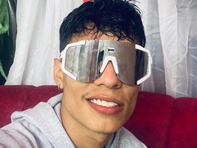 DaironLee with wet black hair, wearing huge reflective white VR goggles, grey hoodie, and small hoop earring, smiling with slightly parted lips, showing small mustache and slight goatee.