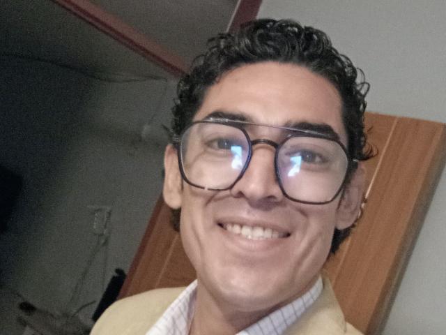 Rahullooo with curly black hair, glasses reflecting light, and a goofy smile, wearing a beige sweater over a white shirt. His ass is not visible.
