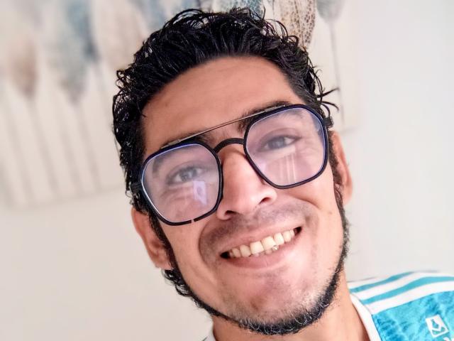 Rahullooo has dark curly hair, a short beard, and is smiling with glasses on. His blue and white shirt is visible. He has a small nasal breathing hole.