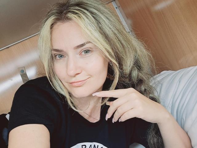 CarmenAutumn has long blonde hair, blue eyes, and a slight smile. She's wearing a black shirt, touching her chin with a finger, and looking directly at the camera.