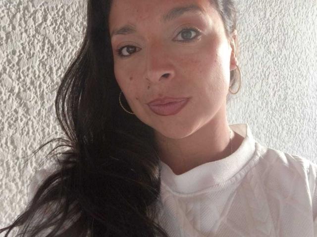 StangelarRivera has brown eyes, long black hair, light skin, small nose, and is wearing a white shirt with a textured pattern. She's also sporting small hoop earrings.