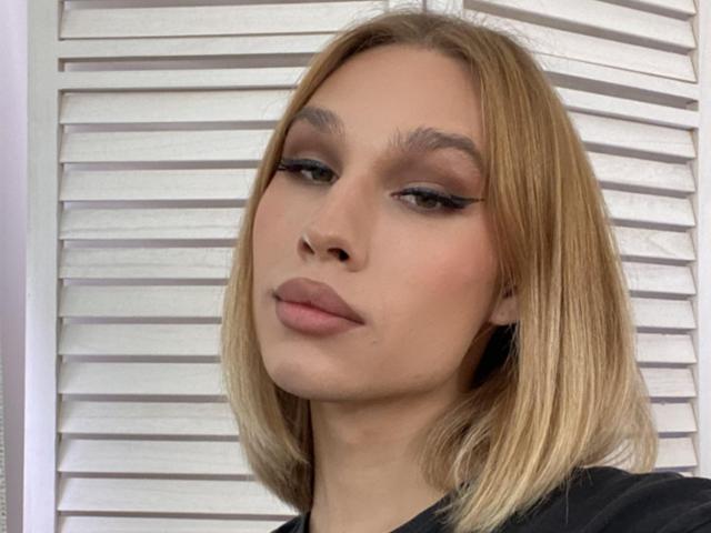 KatalaYeya has blonde bob, subtle eyeliner, and pinkish lipstick, with a slightly upturned nose and neutral expression, wearing a black top.