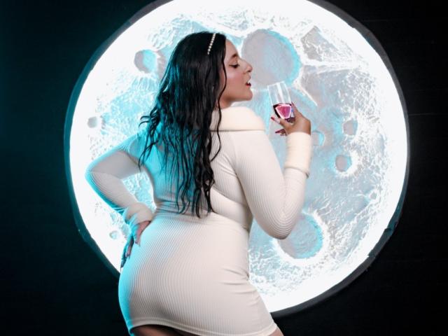 VictoriaRiver with wet black hair, white dress, holding pink drink, standing with ass up, hand on hip, looking over shoulder, moonlit circular light behind.