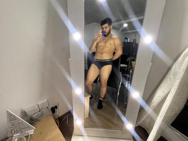 NiganDuquette, muscular, shirtless, wearing only dark gray Calvin Klein briefs, black socks, holding phone, standing in front of mirror with lights, visible ass, taking mirror selfie.