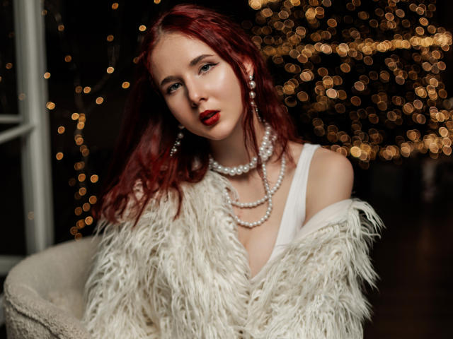 MarieLoving with red hair, wearing a white feather coat, pearl necklace, red lipstick, and earrings, looking seductive with boobs slightly visible under the coat. Bokeh lights in background.