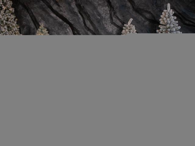 MarieSho with small tits, sitting on a gray pillow, wearing a white shirt, black pants, and white boots, surrounded by frosted Christmas trees.
