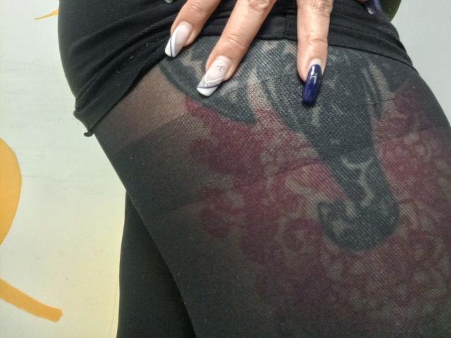 La mano di GinebraVargas, con le sue unghie lunghe, blu e bianche, riposa sul suo sedere coperto da un paio di mutandine nere trasparenti, rivelando un tatuaggio sottostante..