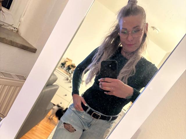 Lexi88-hot with long blonde ponytail, glasses, black top, and ripped jeans, holding phone, mirror selfie, showing small ass, medium tits, and cute face, standing in a room.