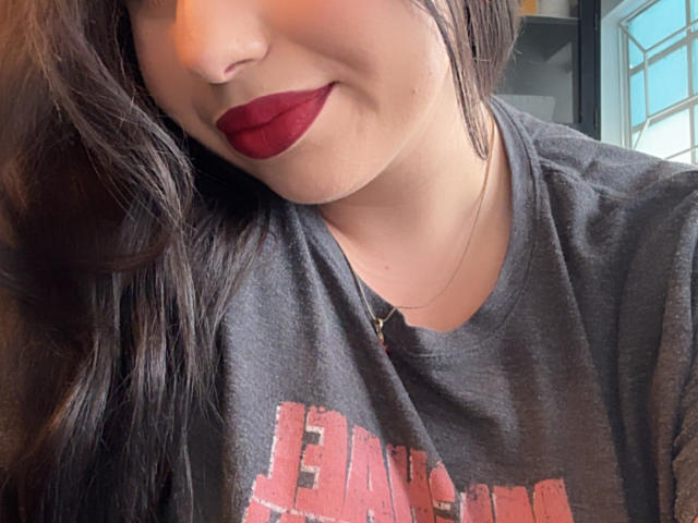 VenusxMusa with red lipstick, dark brown wavy hair, grey t-shirt, and subtle necklace, smiling slightly, showing a cute face, soft skin, and casual style.