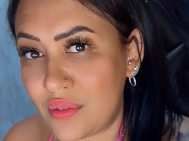 LiraLatinXXX-hot has tan skin, dark eyebrows, long eyelashes, pink lipstick, small nose, and black hair, wearing a pink halter, with silver hoop earrings and a nose ring.