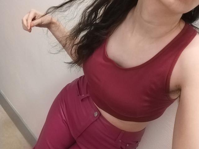  AlexandraSweet with long black hair, wearing a red sports bra and matching high-waisted pants, showing her tits and holding her hair. Her skin is light, and she's standing.