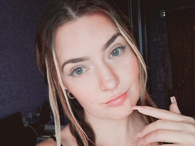 CarmenAutumn has blue eyes, blonde and brown braided hair, and a slight smile with her finger touching her lips. She has light skin and small, pinkish lips.