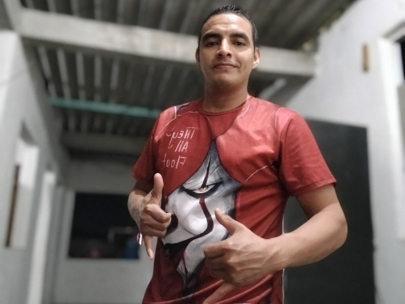 LeonardoHt with short dark hair, wearing a red t-shirt featuring a white, black, and red graphic of a masked face, giving two thumbs up with a slight smile.