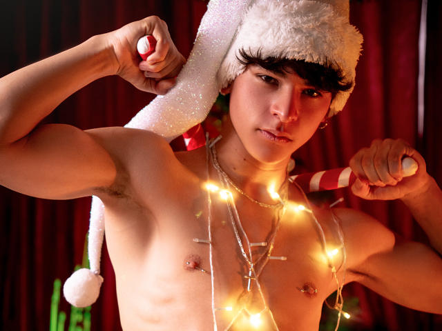 LukeHowlandy, shirtless, wearing a Santa hat, holding a candy cane, with Christmas lights on his chest, flexing his arm, has a cross necklace, and has small nipples.