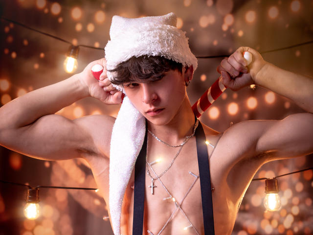 Luke Howlandy, zonder shirt, met een pluizige witte kerstmuts, met lolly's in zijn hand, kerstverlichting op zijn borst, een kruisbeeldketting, gespierd, bruin haar, serieuze uitdrukking, warme bokeh achtergrond..
