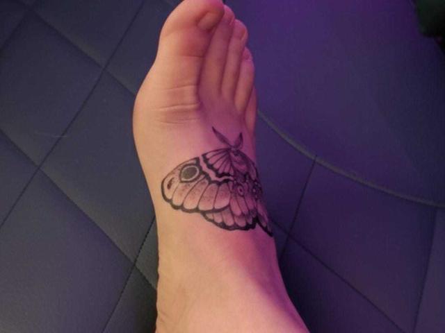 SeleneAna's foot has a black tattoo of a moth with detailed wings and a small dot on its head, located on the outer side of her ankle.