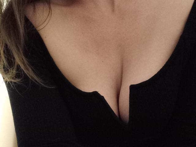 MayaFoxy69's tits in a black top, showing a deep cleavage with her skin tone being light. Her brown hair is partially visible on the left.