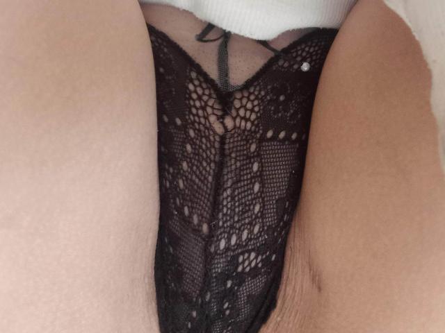 Les culottes en dentelle noire de MayaFoxy69 sont au centre de l'image, montrant un gros plan de son entrejambe avec ses cuisses de chaque côté, mettant en évidence le motif et la texture de la dentelle..