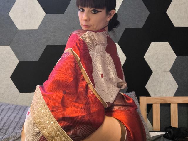 OrianaLaFrancaise in a red kimono with a floral design, sitting with her back to the camera, showing her ass and garter. She has black hair and winged eyeliner.