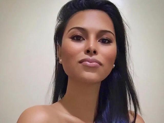 TsLexie-hot has tan skin, long black hair, and wears pearl earrings. She's looking at the camera with a slight smile, showing off her shiny pink lips.