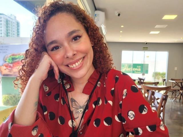 LizzaMonroe-hot, curly red hair, smiling, red polka-dot shirt, hand on cheek, tattoo on chest, white skin, cute, small nose, brown eyes, casual indoor setting, daytime.