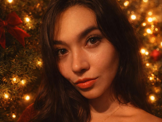 SofieWhite's face with wavy dark brown hair, glossy orange lips, and warm brown eyes, looking slightly to the side, in a softly lit, golden-hued setting.
