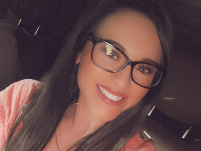 Rubie69 with dark brown hair, wearing black glasses, and a pink shirt, smiling with red lipstick and white teeth, has a cute face and a pretty ass.