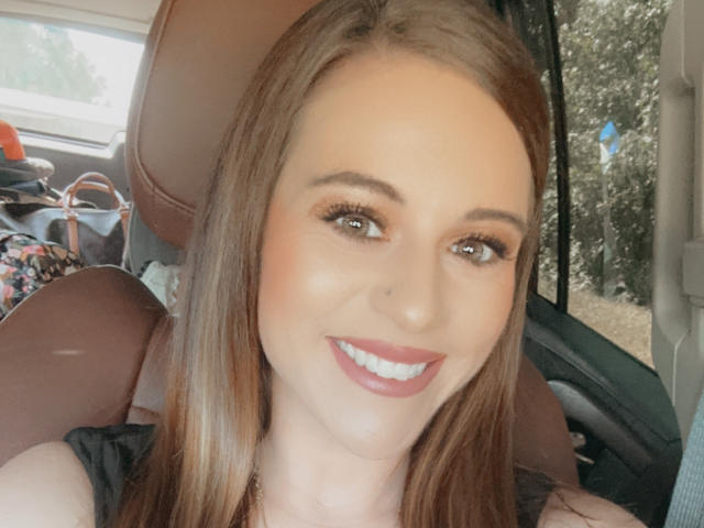Rubie69 has brown eyes, long straight brown hair, and is smiling with red lipstick. She's in a car with brown leather seats. Her tits are not visible.